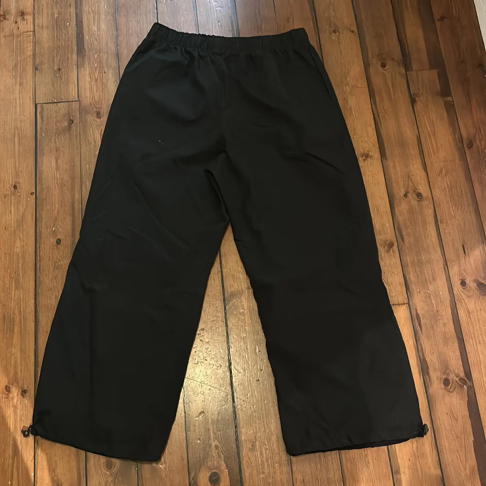 Snygga svarta byxor med resårmidja och justerbara benslut. Perfekta för en avslappnad stil. Byxorna har en loose passform och är tillverkade i ett lätt material.. Farkut & Housut.