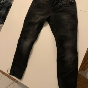 Svarta jeans från Replay - Snygga svarta Replay Anbass jeans med en modern passform. De har en klassisk femficksdesign och subtila slitningar för en trendig look. Perfekta för en stilren vardagsoutfit. Midje storleken är 30 men sitter mer som 29