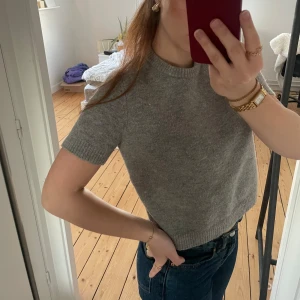 Grå stickad tröja/t-shirt/topp - Säljer en stilren grå stickad tröja med korta ärmar. Perfekt för en avslappnad look. Tröjan har en rund halsringning och ribbade kanter.❣️❣️