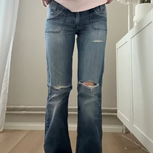 Bootcut låga lee jeans - Snygga blå jeans med slitningar på knäna och en avslappnad passform. De har en klassisk femficksdesign och är perfekta för en casual look. Jeansen har en lågmidjad stil och är tillverkade i ett bekvämt denimtyg.