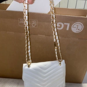 Vit quiltad axelväska med guldkedja - Snygg vit axelväska med quiltat mönster och guldkedja som axelrem. Väskan har en stilren design med ett praktiskt magnetlås. Perfekt för att ge en elegant touch till din outfit.