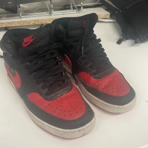 Nike Air Jordans i svart och rött - Snygga Nike Air Jordans i klassisk svart och röd färgkombination. Skorna har en hög modell med snörning och den ikoniska Nike-loggan på sidan. Perfekta för dig som vill ha en stilren och sportig look.