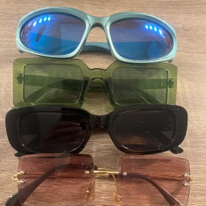 Fyra par solglasögon i olika stilar - ALLA för 30kr. Säljer fyra par solglasögon: ett par med blå ovala linser och ljusblå bågar, ett par med gröna rektangulära linser och gröna bågar, ett par med svarta rektangulära linser och svarta bågar, samt ett par med bruna linser och guldiga, tunna bågar. Det är lite damm på dem på bilderna men de har inga defekter och endast de bruna är använd. 