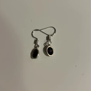 Silvriga örhängen med vinröd sten - Eleganta silvriga örhängen med en oval svart sten. Perfekta för att ge en stilren touch till din outfit. De har en enkel krok för enkel användning.Tvättar innan skickar 