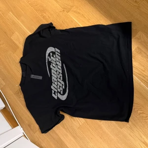 Svart t-shirt från FSBN - Snygg svart t-shirt från FSBN med texten 'chaotic system' i ett coolt, glittrigt mönster på framsidan. T-shirten har en relaxed fit och är perfekt för en avslappnad stil.