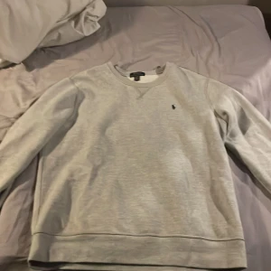 Grå sweatshirt från Polo Ralph Lauren - Säljer en klassisk grå sweatshirt från Polo Ralph Lauren med rund hals och det ikoniska broderade logotypen på bröstet. Perfekt för en avslappnad stil. Tröjan har långa ärmar och ribbade muddar. Aldrig använd