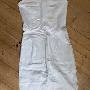 Vit axelbandslös klänning från Bik Bok - Snygg vit axelbandslös klänning från Bik Bok. Perfekt för sommarens fester med en figurnära passform och dragkedja i ryggen. Klänningen har en stilren design som framhäver silhuetten. Finns även band som går att sätta fast om man föredrar det.