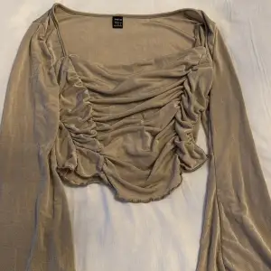 Snygg beige topp från Shein med långa ärmar och rynkade detaljer framtill. Perfekt för en stilren look med en touch av elegans. Toppen har en mjuk och glansig finish.
