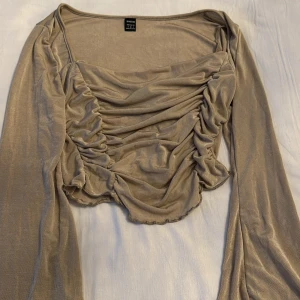 Beige långärmad topp från Shein - Snygg beige topp från Shein med långa ärmar och rynkade detaljer framtill. Perfekt för en stilren look med en touch av elegans. Toppen har en mjuk och glansig finish.