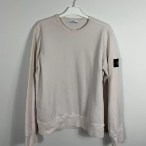 Beige tröja från Stone Island - Säljer en stilren beige tröja från Stone Island med deras ikoniska märke på ärmen. Tröjan har en rund hals och långa ärmar, perfekt för en avslappnad look. Köpt på Sweet&Tender i Helsingborg 
