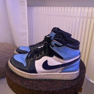 Nike Air Jordans i blå och svart - Snygga Nike Air Jordans i en cool kombination av blått och svart. Skorna har en klassisk hög design med snörning och den ikoniska Nike-loggan på sidan. Perfekta för dig som vill ha en stilren och sportig look.