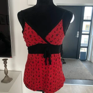 Röd och svart linne från Bka Forever - Trendig rött linne med svart mönster av små katter från Bka Forever. Toppen har en knytning på framsidan och en bekväm passform. 