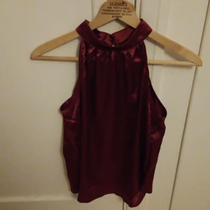 Vinröd ärmlös topp från Shein - Snygg vinröd ärmlös topp från Shein i ett glansigt material. Perfekt för en kväll ute eller en speciell tillställning. Toppen har en elegant design med hög hals och ett mjukt fall.