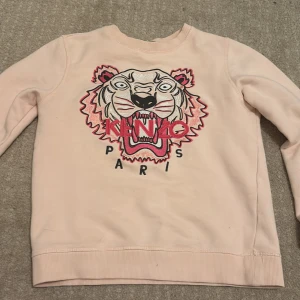 Rosa sweatshirt från Kenzo - Säljer en snygg rosa sweatshirt från Kenzo med ett coolt tigertryck och texten 'Kenzo Paris' på framsidan. Tröjan har långa ärmar och en rund halsringning. Perfekt för en trendig look! 🐯