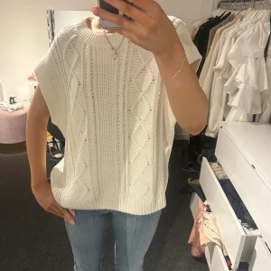 Vit stickad topp med öppen rygg - Säljer en snygg vit stickad topp med ett unikt mönster och öppen rygg. Toppen har korta ärmar och en knytning bak som ger en cool look. Perfekt för lager-på-lager-stil eller att bära som den är. Passar till både jeans och kjol!