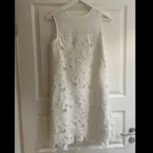 Vit blommig klänning från Oxygene - Säljer en elegant vit klänning från Oxygene med vackra blommiga spetsdetaljer. Klänningen är ärmlös och har en stilren design som passar perfekt för sommarens festligheter. Passar bra som S och XS med!💕