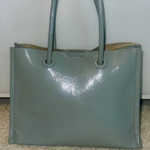 Grå axelväska i syntet - Snygg grå axelväska i glansigt syntetmaterial. 