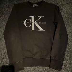 Brun sweatshirt från Calvin Klein Jeans - Säljer en snygg brun sweatshirt från Calvin Klein Jeans med det ikoniska CK-logotypen tryckt på framsidan. Tröjan har en klassisk rund halsringning och ribbade muddar vid ärmslut och nederkant. Perfekt för en stilren och avslappnad look. Pris kan diskuteras vid snabb affär!🙌🏻