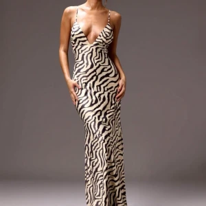 Zebramönstrad långklänning med öppen rygg - Snygg zebramönstrad långklänning med djup v-ringning och smala axelband. Klänningen har en elegant öppen rygg med snörningsdetaljer som ger en unik look. Perfekt för att sticka ut på festen!