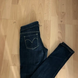 Mörkblå jeans från Levi's - Snygga mörkblå jeans från Levi's med en klassisk femficksdesign. De har en knappgylf och är i modellen 'Slight Curve'. Perfekta för en stilren look.