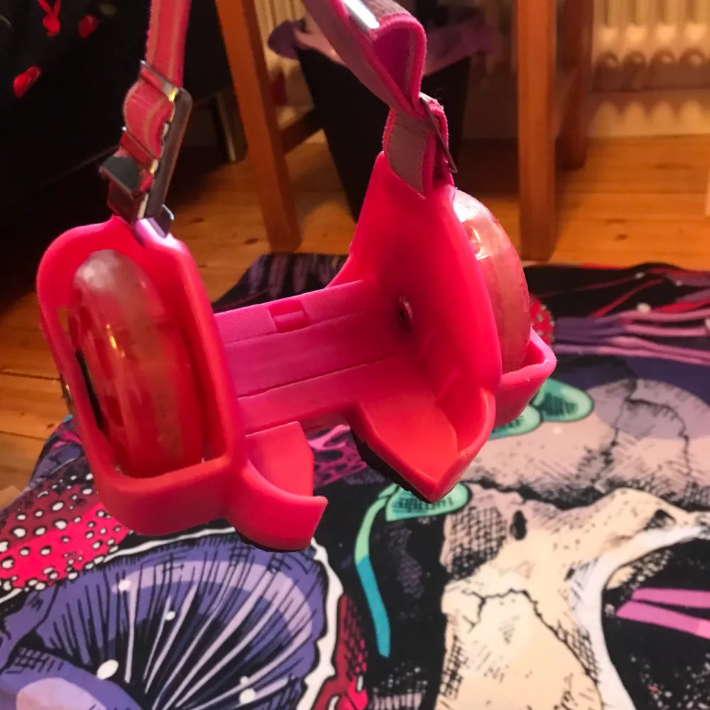 Säljer ett par rosa rullskridskor med justerbara remmar. De har två hjul på varje sko och är designade för att enkelt kunna sättas på vanliga skor. Perfekta för att glida runt med stil!. Kengät.