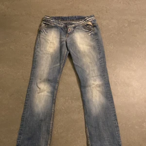 Blå jeans från Replay - Snygga blå jeans från Replay med coola slitningar och broderade detaljer på bakfickorna. Innerbenslängd: 77 Midjemått: ca 36 