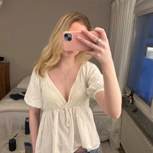 Vit blus med knytning - Säljer en söt vit blus med v-ringning och knytning framtill. Blusen har korta ärmar och en luftig passform, perfekt för varmare dagar. Den är tillverkad i ett lätt och bekvämt material.