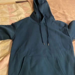 Mörkblå hoodie - Säljer en stilren mörkblå hoodie med justerbar huva och praktisk magficka. Perfekt för en avslappnad look. Materialet känns mjukt och bekvämt mot huden.