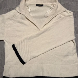 Vit stickad tröja från Gina Tricot - Säljer en stilren vit stickad tröja från Gina Tricot med svarta detaljer vid ärmslut och nederkant. Tröjan har en unik krage och långa ärmar. Perfekt för en avslappnad och trendig look.