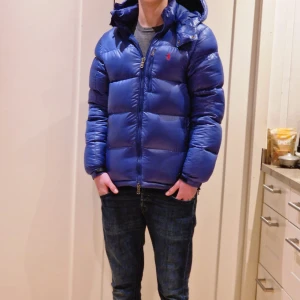 Blå pufferjacka från Ralph Lauren - Säljer en snygg blå pufferjacka från Ralph Lauren. Storlek XS men passar S Jackan har en dragkedja framtill och en liten broderad logga på bröstet. Den är perfekt för kalla dagar med sin vadderade design och har en justerbar huva för extra skydd. Pris kan diskuteras. Kontakta vid minst fundering. På bilderna är jag 175cm
