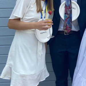 Vit klänning med volangdetaljer - Charmig vit klänning med korta ärmar och volangdetaljer vid fållen. Klänningen har en knytning i midjan som ger en fin passform. Lite öppen i ryggen också. Perfekt för studenten eller somriga tillfällen! Använd en gång