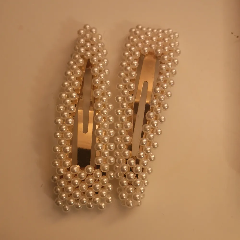 Två eleganta hårspännen dekorerade med vita pärlor. Perfekta för att ge en stilfull touch till din frisyr. En guldig bas som ger en lyxig känsla.. Asusteet.