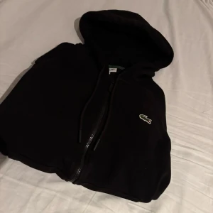 Lacoste Hoodie M  - Säljer en mycket fet svart lacoste hoodie med zip. Riktigt fet och passar till mycket. Köpt i Danmark i lacoste butiken för ca 1500kr. Den är i bra skick.