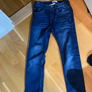 Blå jeans från Lindex - Snygga blå jeans från Lindex med en klassisk femficksdesign. De har en knappgylf och bälteshällor, vilket gör dem perfekta för en avslappnad stil. Märket 'Detroit' syns på baksidan.
