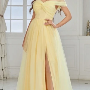 Gul långklänning med slits - Elegant gul långklänning med offshoulder-design och en vacker slits framtill. Klänningen har en omlott-detalj vid bysten som ger en sofistikerad look. Perfekt för speciella tillfällen.