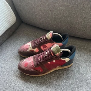 Valentino Rockrunner  - Snygga Valentino Rockrunner sneakers i ett unikt camouflage-mönster med nyanser av röd och blå. Skorna har en klassisk snörning och är tillverkade i en kombination av skinn och syntetmaterial. Perfekta för att ge din outfit en cool touch.
