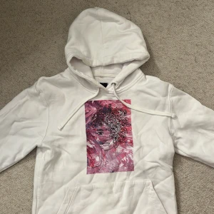 Vit hoodie från The Cool Elephant - Säljer en vit hoodie från The Cool Elephant med en unik konstnärlig design i rosa och lila på framsidan. Hoodien har en klassisk passform med långa ärmar och en bekväm huva med dragsko. Perfekt för en avslappnad stil.