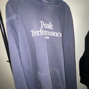 Blå hoodie från Peak Performance - Säljer en snygg blå hoodie från Peak Performance med vit logga på bröstet. Den har en klassisk design med en stor huva och en praktisk magficka. Perfekt för en avslappnad stil. Storlek m men skulle säga att den passar s eller xs mer 