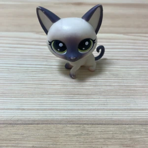 PetShopp - En söt liten leksaksfigur föreställande en katt med stora gröna ögon. Katten har en vit kropp med mörka detaljer på öron, ansikte och svans. Perfekt för samlare eller som leksak för barn.