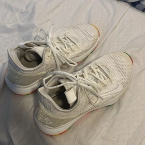 Lebron witness 4’s - Snygga vita basketskor med en unik färgglad sula i rött, grönt, gult och blått. Skorna har ett stickat mönster och snörning framtill. På baksidan finns en dekorativ lejonemblem. Perfekta för att ge din stil en färgklick!