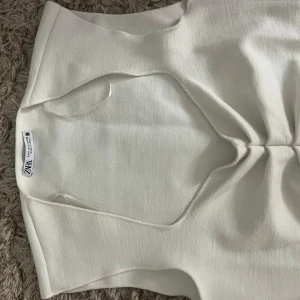 Vit topp från Zara - Snygg vit topp från Zara med en stilren design och v-ringad detalj framtill. Perfekt för en elegant look. Toppen är ärmlös och har en figurnära passform som framhäver silhuetten.