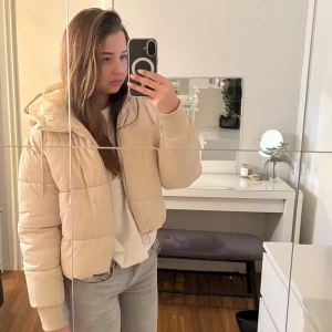 Beige pufferjacka - Säljer en supermysig beige pufferjacka i mycket bra skick. Den är perfekt för höst och vinter med sin varma vaddering och huva. Jackan har en dragkedja framtill och ribbade muddar vid ärmsluten. Den är i en normal passform och passar perfekt till vardagsoutfiten. Perfekt för kyliga dagar! 🍂🧡