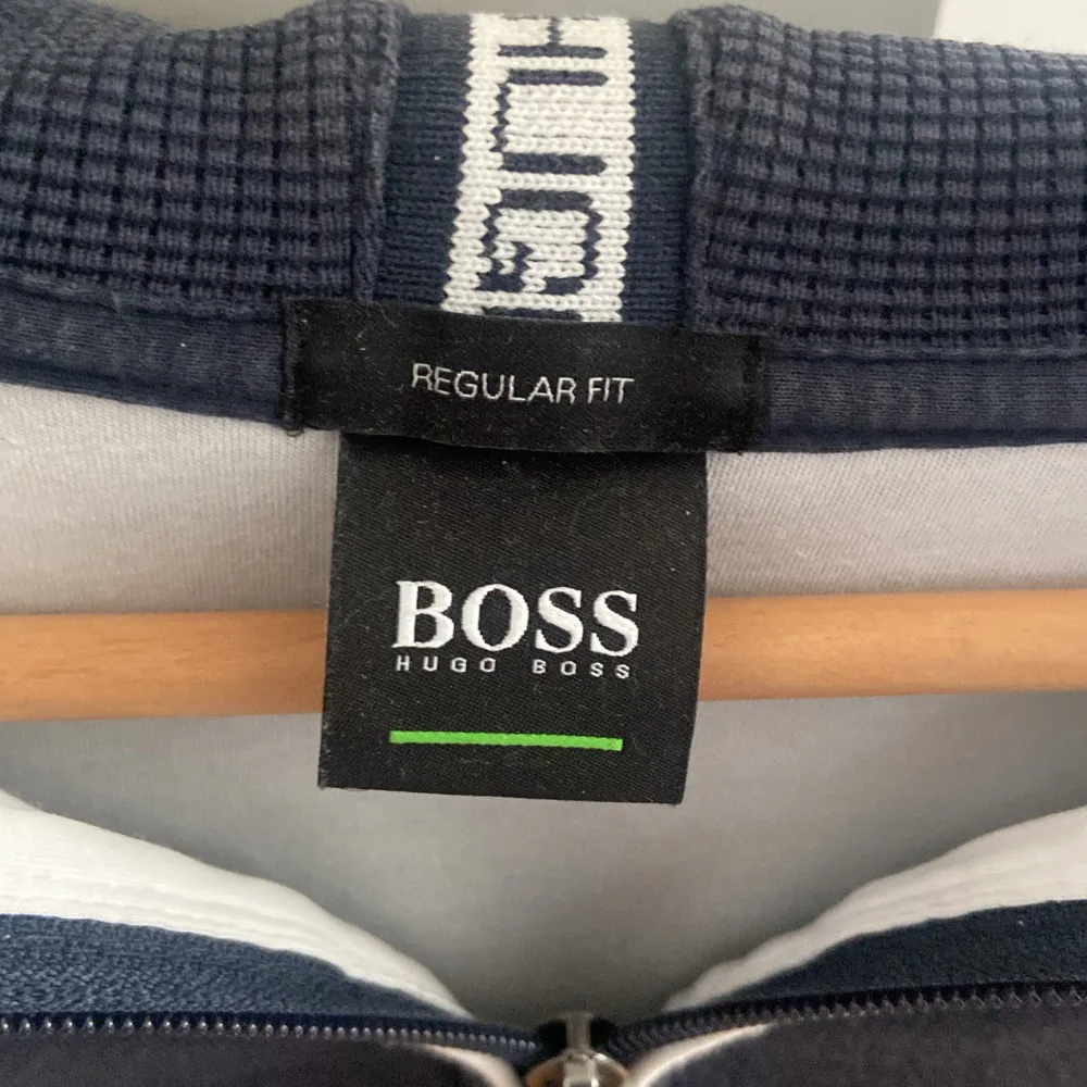 Säljer en snygg mörkblå hoodie från Hugo Boss i regular fit. Den har en dragkedja framtill och en klassisk logga på bröstet. Perfekt för både vardag och träning. Grymt skön och stilren!. Tröjor & Koftor.