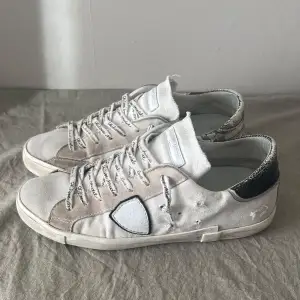 Säljer ett par Philippe Model sneakers i vit mocka med coola slitningar och vita detaljer. Skorna har en snygg glittrig häl och klassisk snörning. Perfekta för en avslappnad stil med en touch av lyx. Sulan har tappat färgen lite. De är i Okej skick och kommer med originalkartong. Dom är såklart äkta!