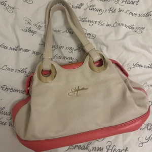 Beige och rosa axelväska - Säljer en snygg axelväska från Stefano i beige och rosa. Väskan har guldfärgade detaljer och en praktisk dragkedja. Perfekt för både vardag och fest! 👜✨