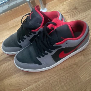 Nike Air Jordans i grått och rött - Säljer ett par Nike Air Jordans i grått och rött. Skorna har en snygg kombination av grå mocka och svart syntet med röda detaljer och sula. Perfekta för både vardag och fest! De är i bra skick med lite slitage på sulan. Passar perfekt för dig som vill ha en stilren och sportig look.