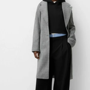 Grå kappa - Snygg och stilren grå kappa i ull. Perfekt för höst och vinter med sin långa design och klassiska look. Den har långa ärmar och en rak passform som ger en elegant siluett. Passar både till vardags och festliga tillfällen. Den är sällan använd och ser ut precis som ny.