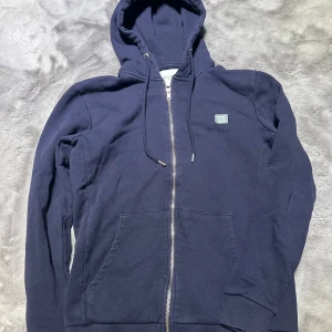 Mörkblå hoodie med dragkedja - Säljer en snygg mörkblå hoodie från Les Deux. Den har en dragkedja framtill och en liten logga på bröstet. Perfekt för kyliga dagar och passar till det mesta. Den är i bra skick och superbekväm att ha på sig. Hör av dig om du är intresserad!