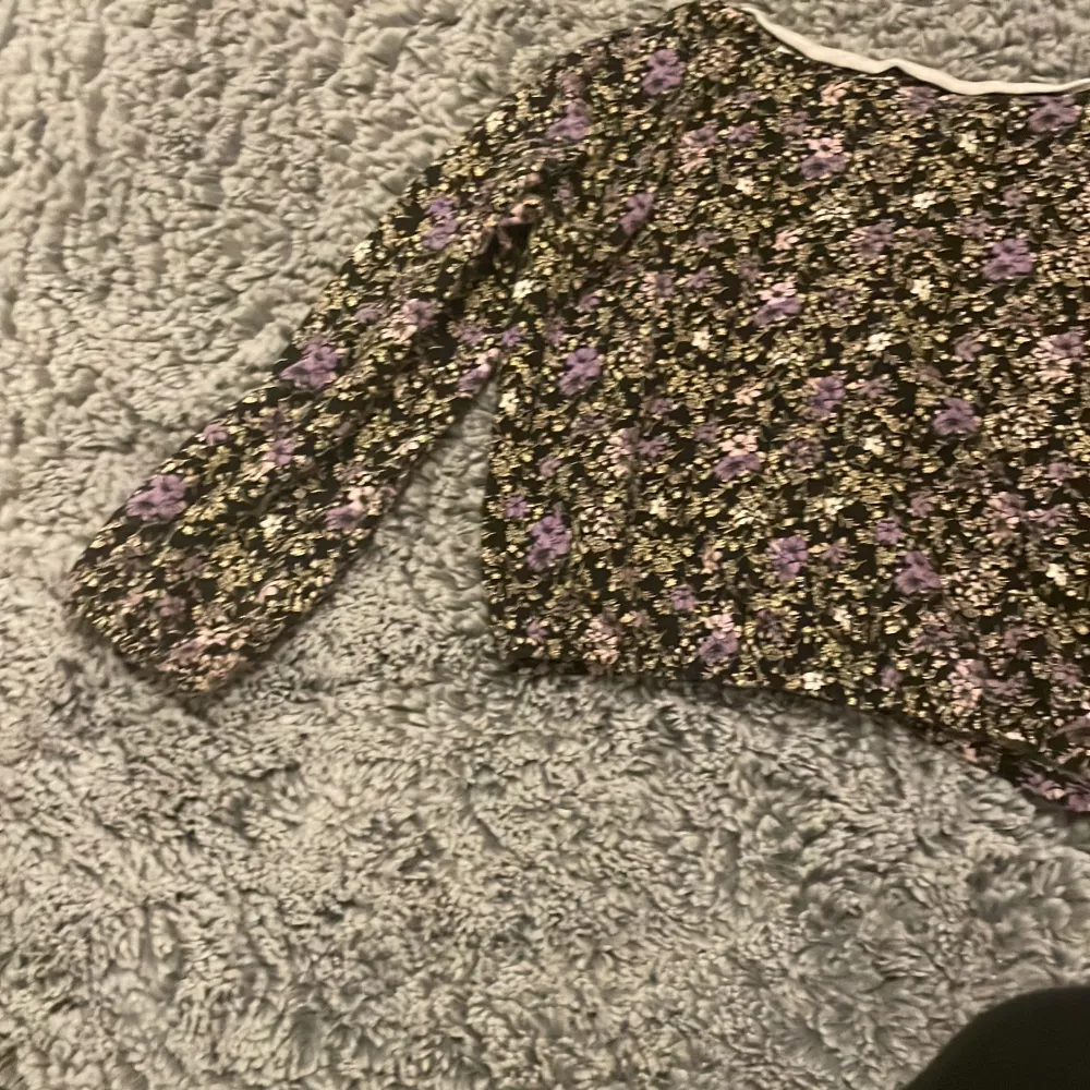 Säljer en superfin blommig topp med lång ärm. Den har ett mönster i lila och vitt på en svart bakgrund. Perfekt för både vår och höst! Toppen är i bra skick och passar till både jeans och kjol. 🌸. Tröjor & Koftor.