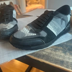 Valentino rockrunners - Säljer ett par snygga Valentino sneakers i svart och grått med coolt kamouflagemönster. Storlek 43, Skorna har en robust sula och är i bra skick. Perfekta för en casual look eller en utekväll. De har snörning och är gjorda i en mix av skinn och syntetmaterial.       Nypris 8500kr 